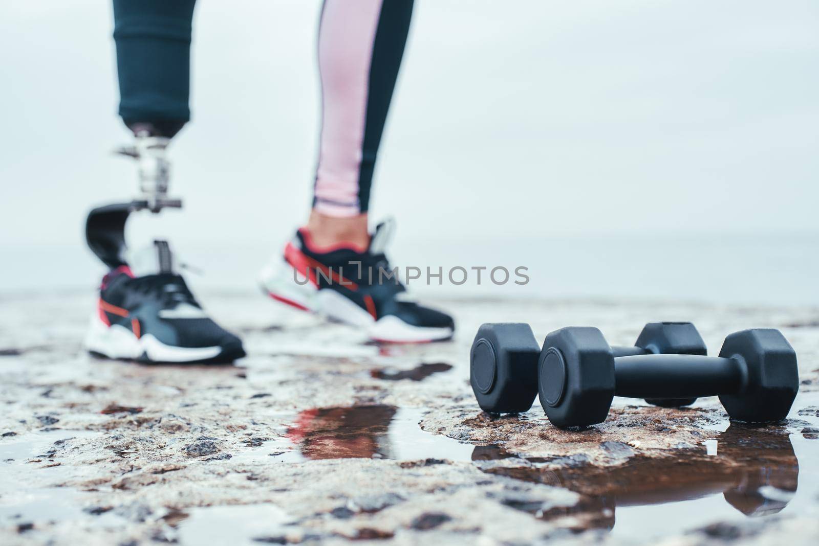 Strong and healthy. Cropped image of woman with prosthetic leg and dumbbells lying in front of the sea. by friendsstock