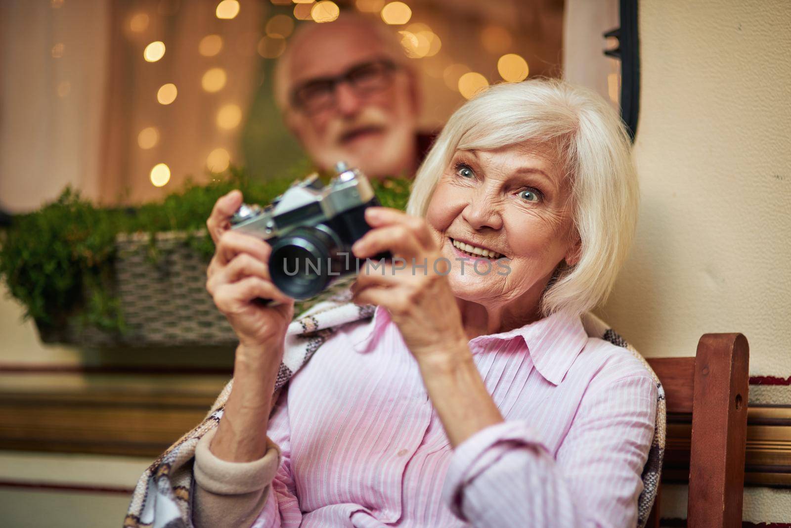 Smiling beautiful woman holding camera and going to make photo with her husband in the motorhome on the background. Travel concept