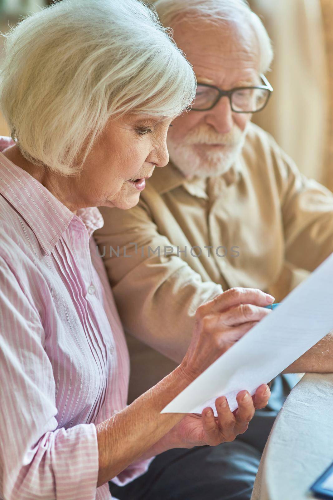Close up of worried senior couple checking their account at home while holding documents. Family and household concept