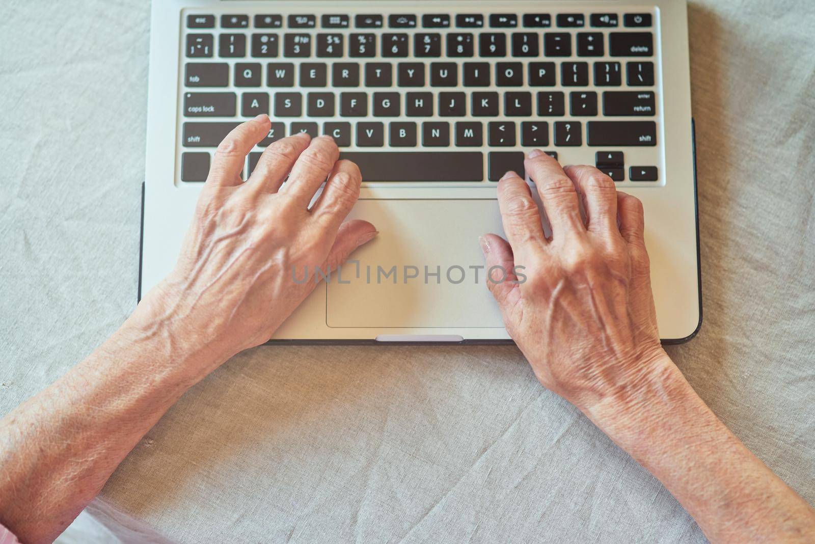 Top view of wrinkled female hands typing on laptop. Domestic lifestyle concept