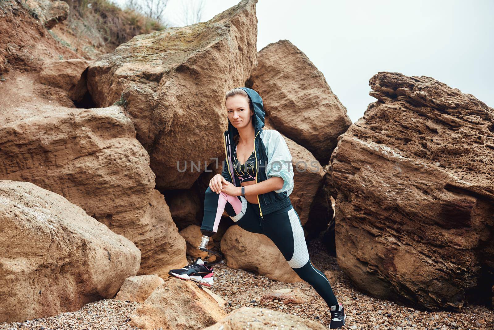 Sport is my way of life. Beautiful and young disabled athlete woman in sportswear with prosthetic leg standing on the beach after morning workout and looking at camera. Sport concept. Sport outside. Disabled Sportsman.