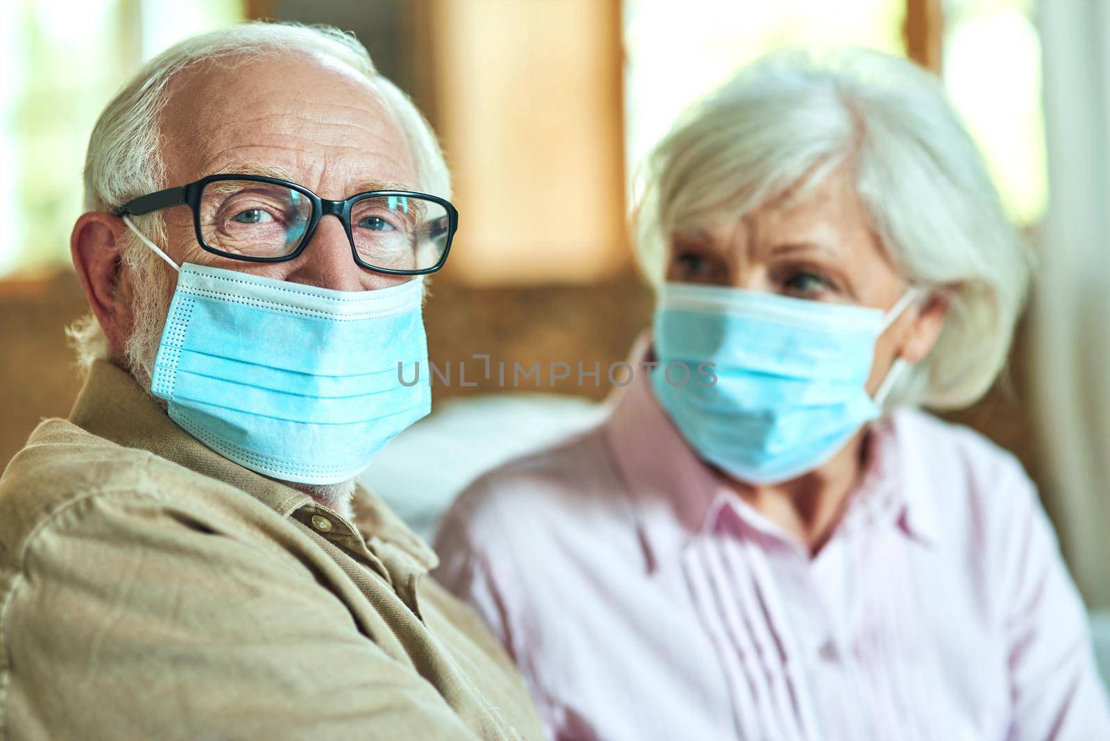 Senior man in glasses sitting next to his wife and using masks by friendsstock