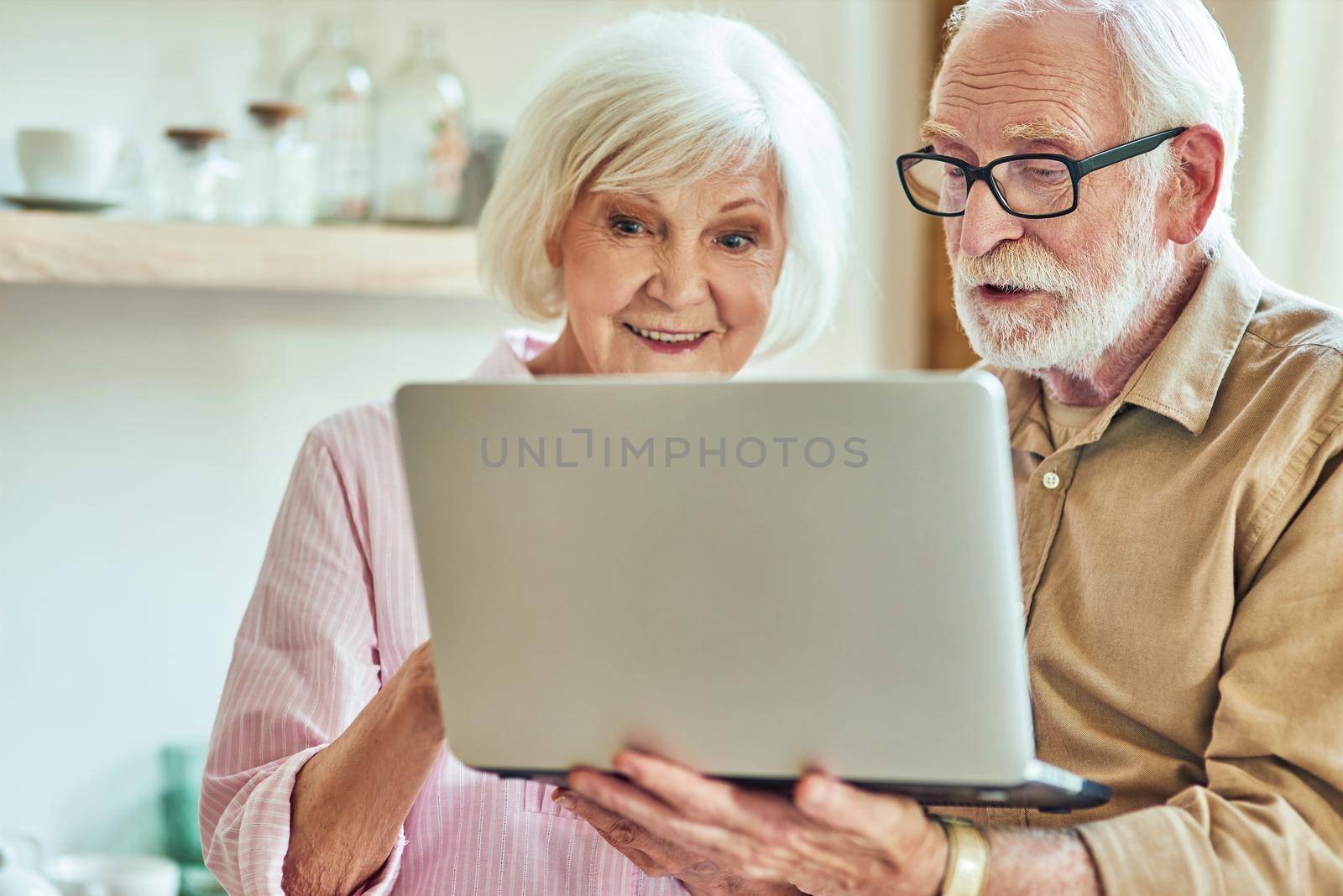 Waist up of elderly couple standing together and holding laptop in hands while looking at screen. Lifestyle concept