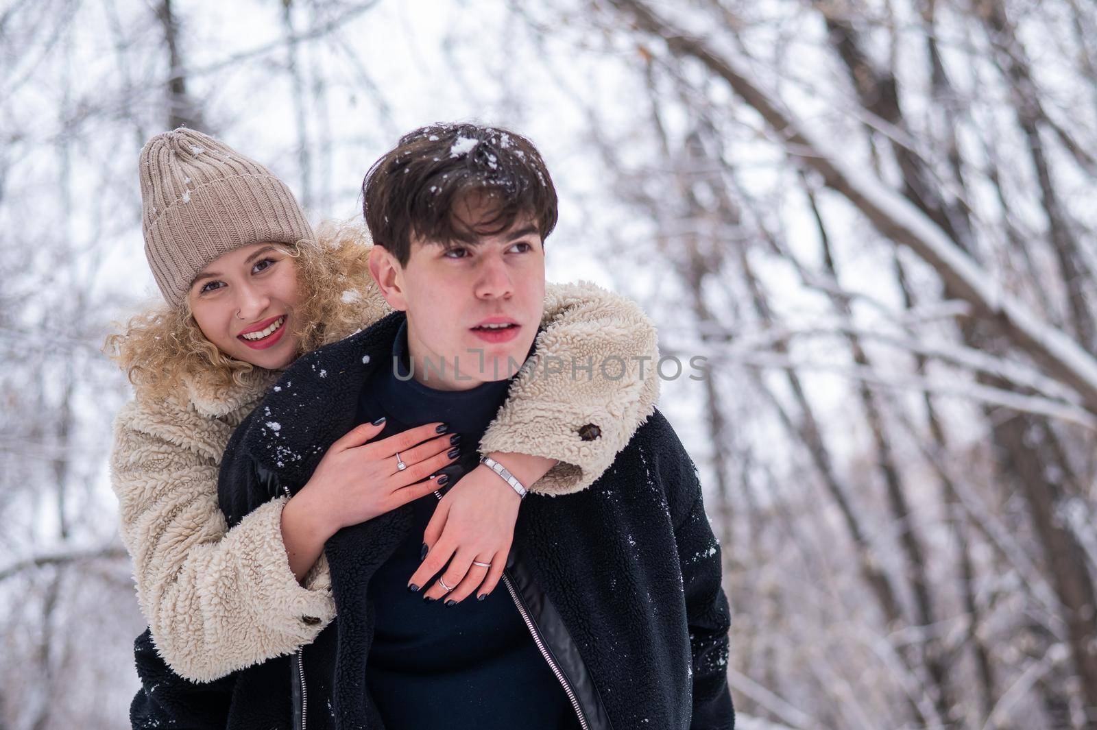 A young couple walks in the park in winter. Guy and girl hugging outdoors