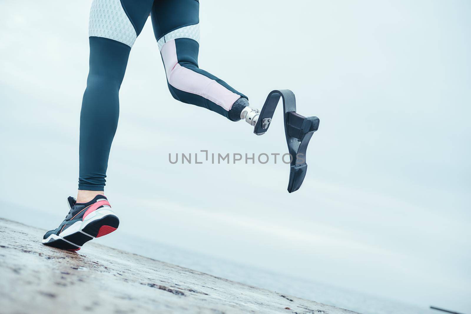 Life is in your hands. Cropped photo of disabled woman with bionic leg in sportswear is running on the beach in the morning. Sport concept. Disabled Sportsman