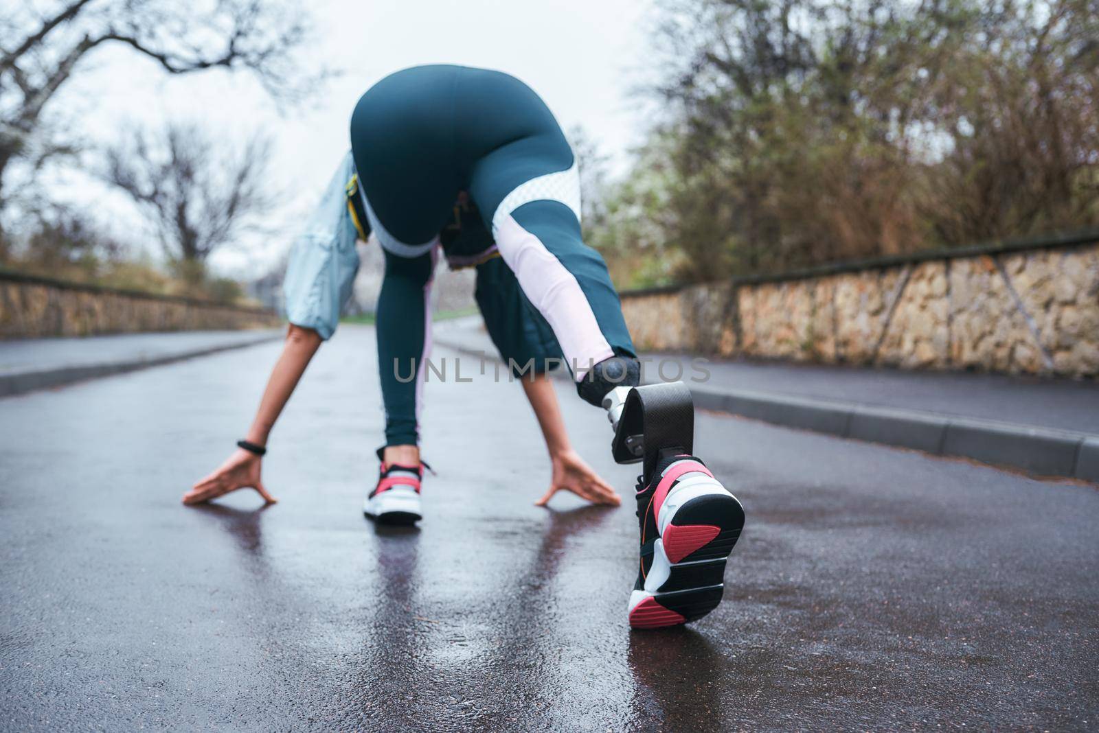 Get better everyday Back view of disabled athlete woman in sportwear with prosthetic leg getting ready to run outdoor by friendsstock