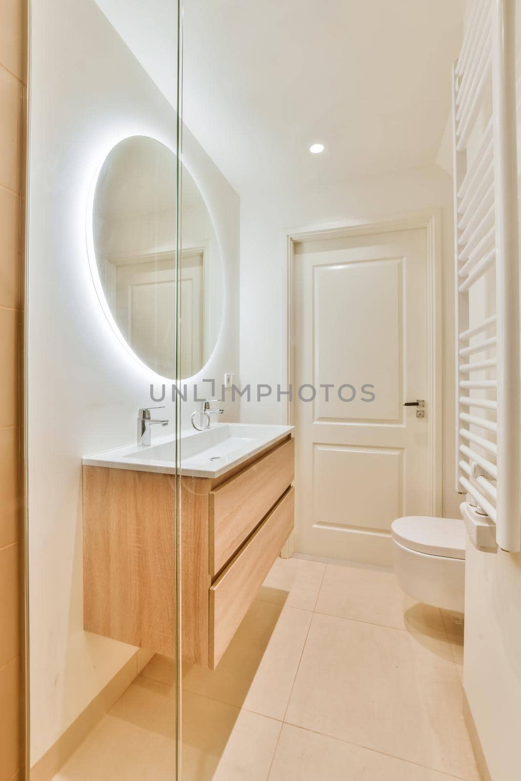 Luxurious bathroom with beige tiled floor and round large mirror with lighting