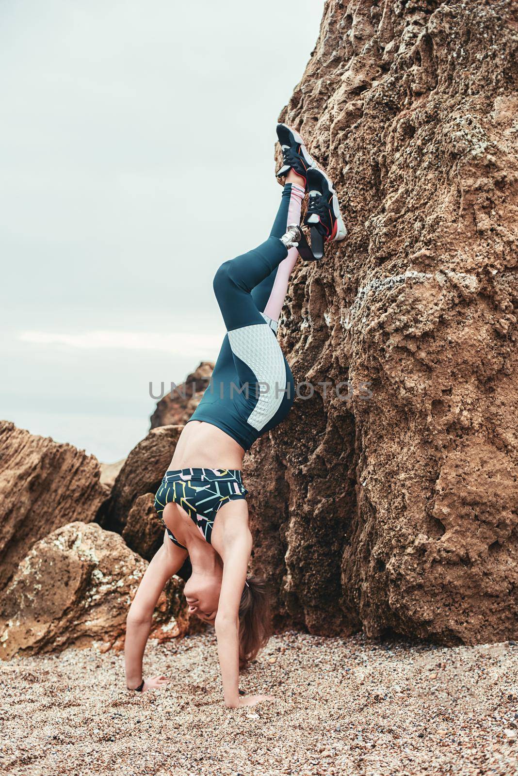 Vertical photo of strong disabled woman working out outdoors and doing handstand exercise on the beach. by friendsstock