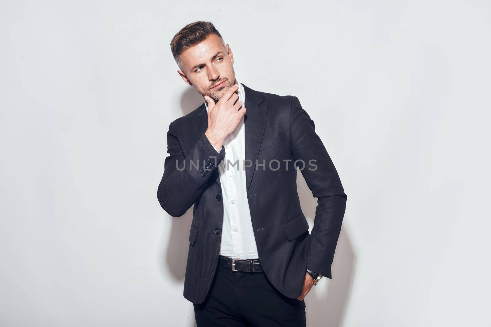 Handsome man. Bearded businessman in classic suit touching his chin and looking away while standing against grey background by friendsstock