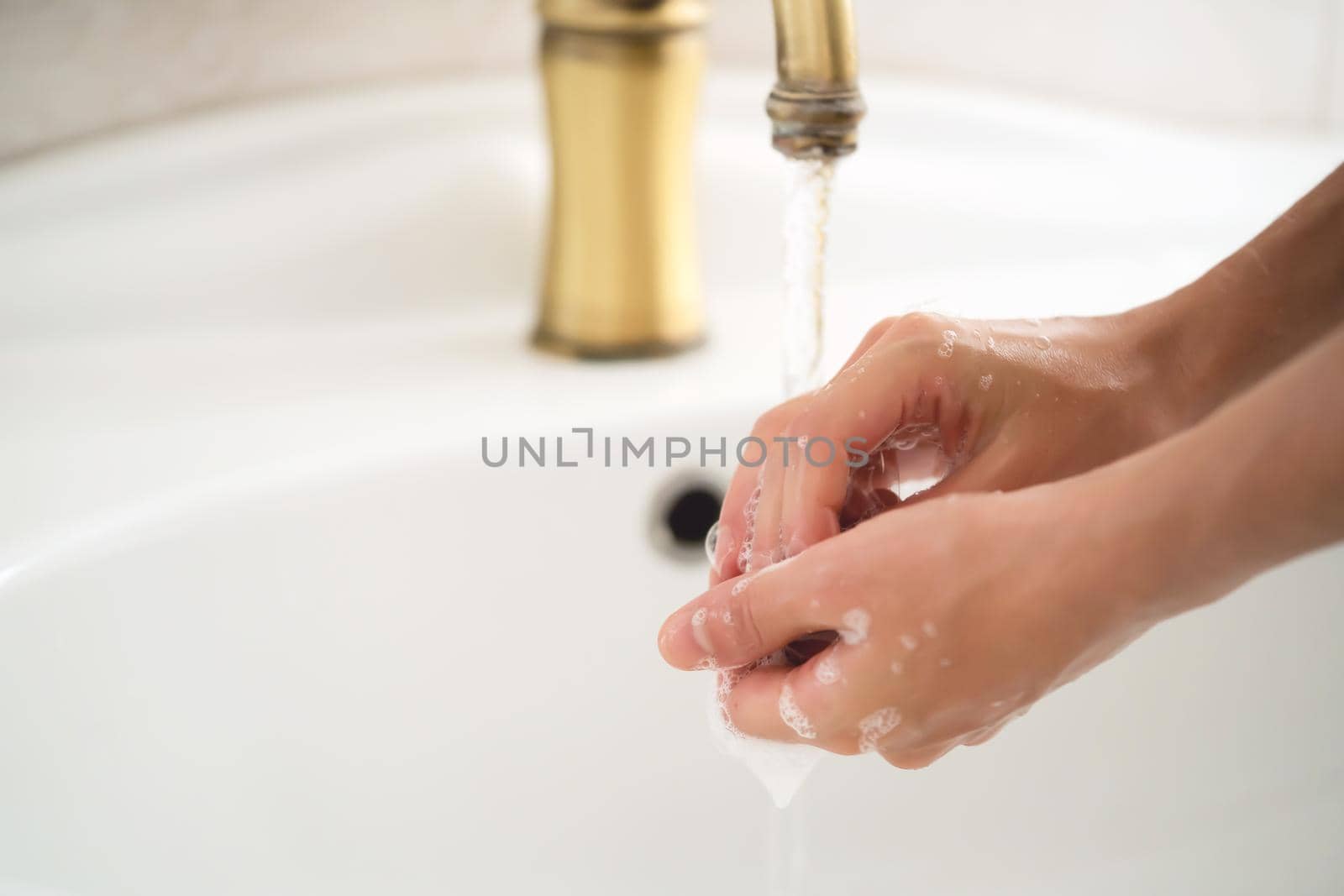 A young girl washes her hands thoroughly with soap under water in the bathroom, close-up view.