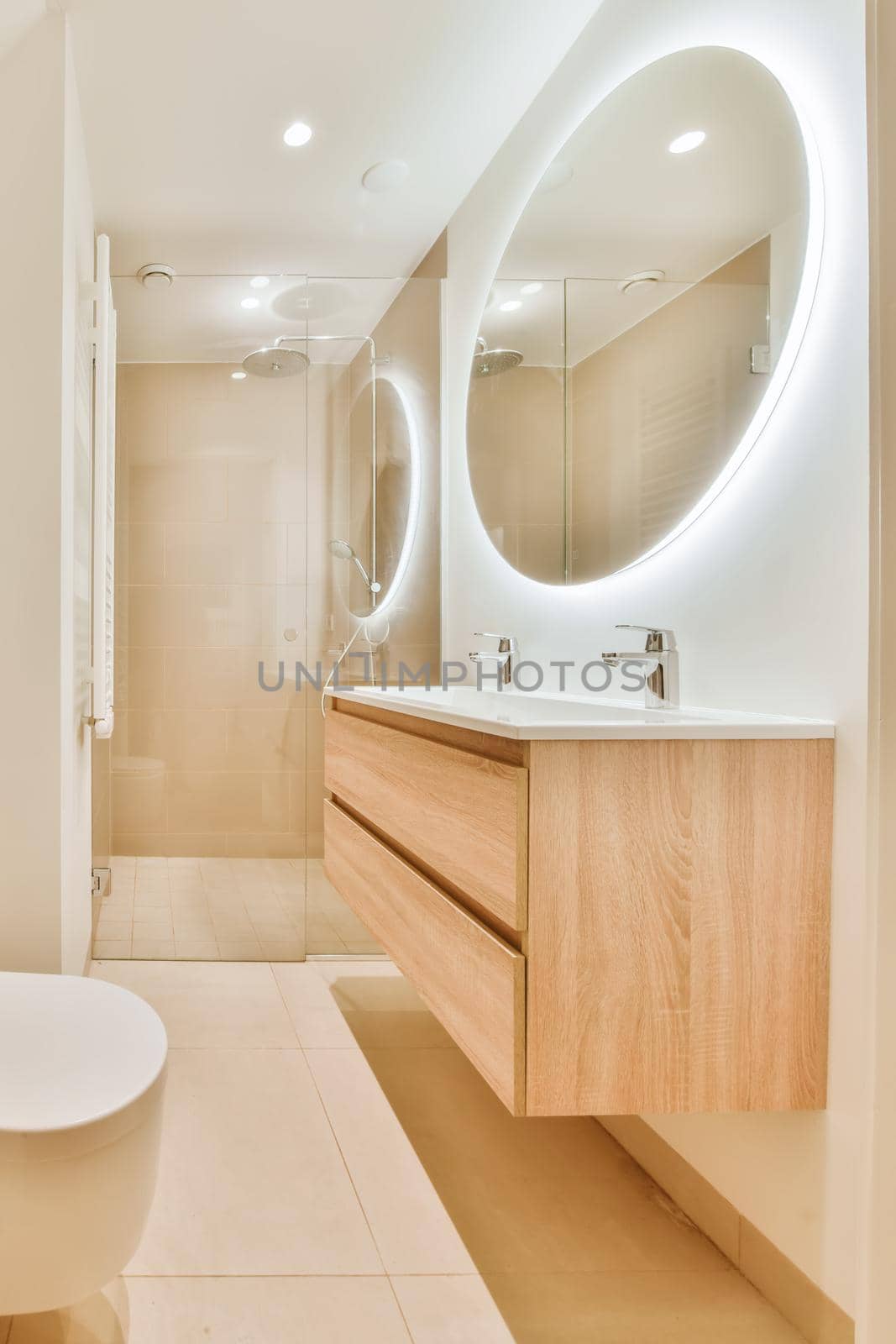 Luxurious bathroom with beige tiled floor and round large mirror with lighting