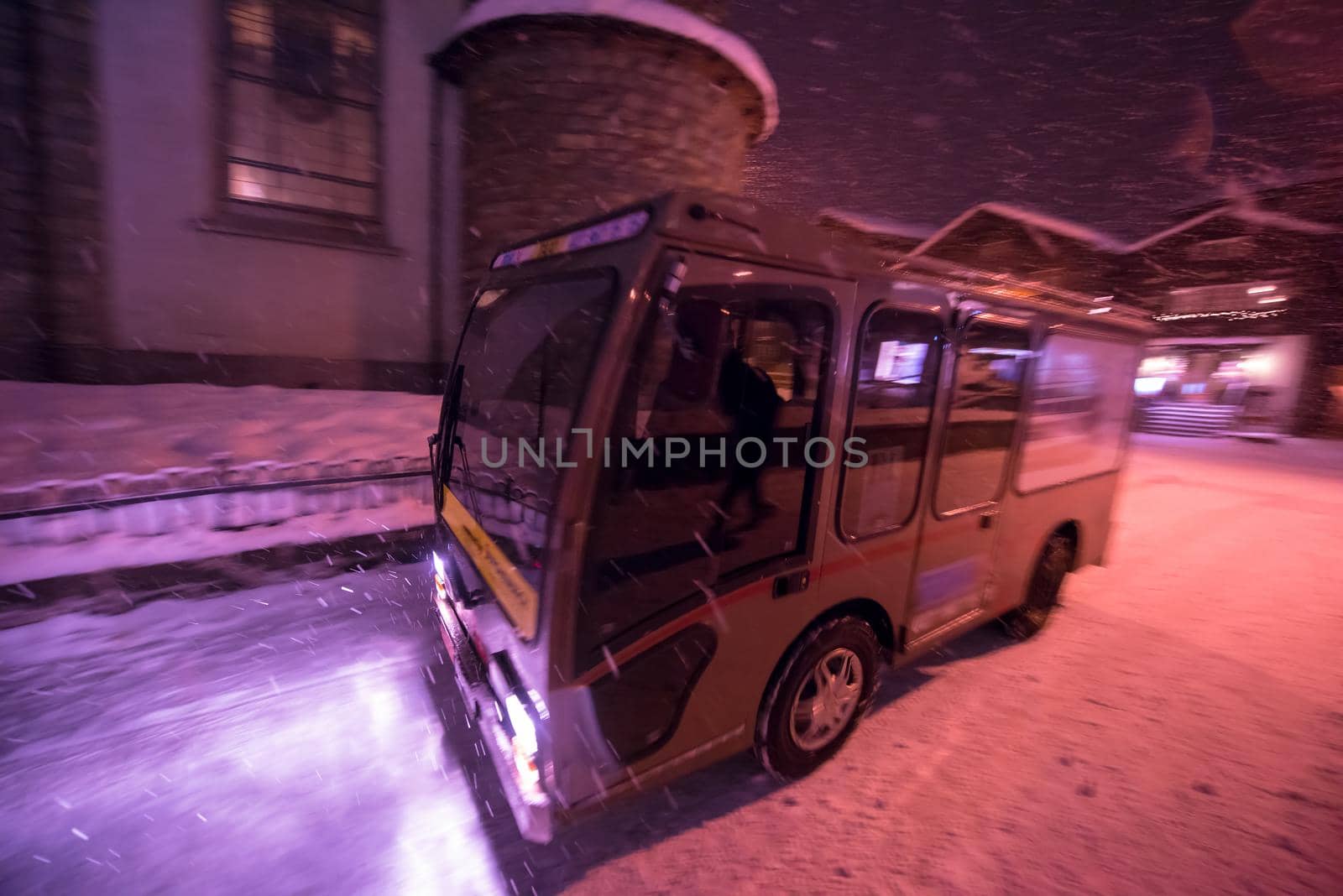 Electric taxi bus on snowy streets in the car-free Alpine mountain village at cold winter night