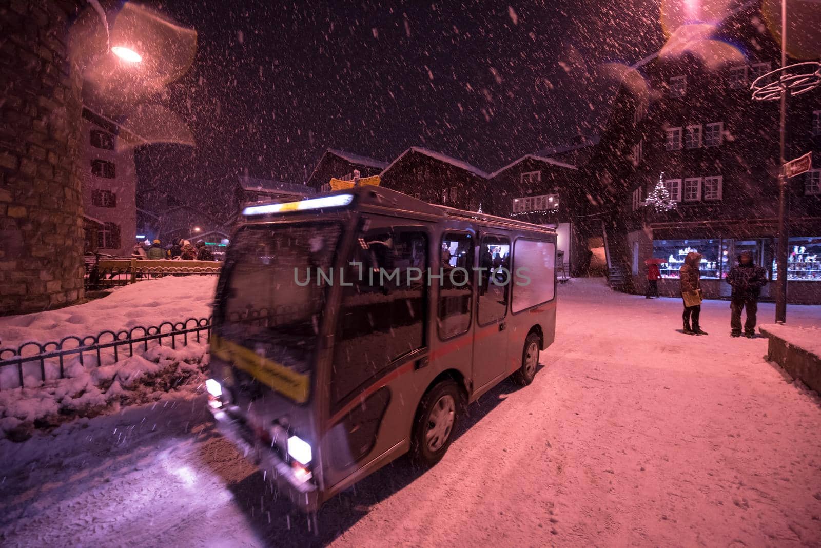 Electric taxi bus on snowy streets in the car-free Alpine mountain village at cold winter night