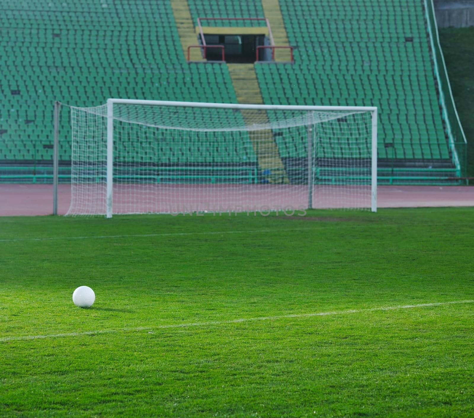 Soccer ball on grass at goal and stadium in background by dotshock