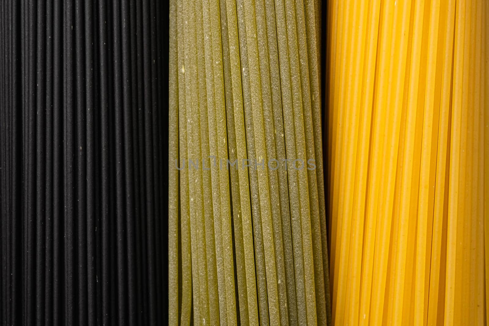 Colored spaghetti raw dry set, on black dark stone table background, top view flat lay