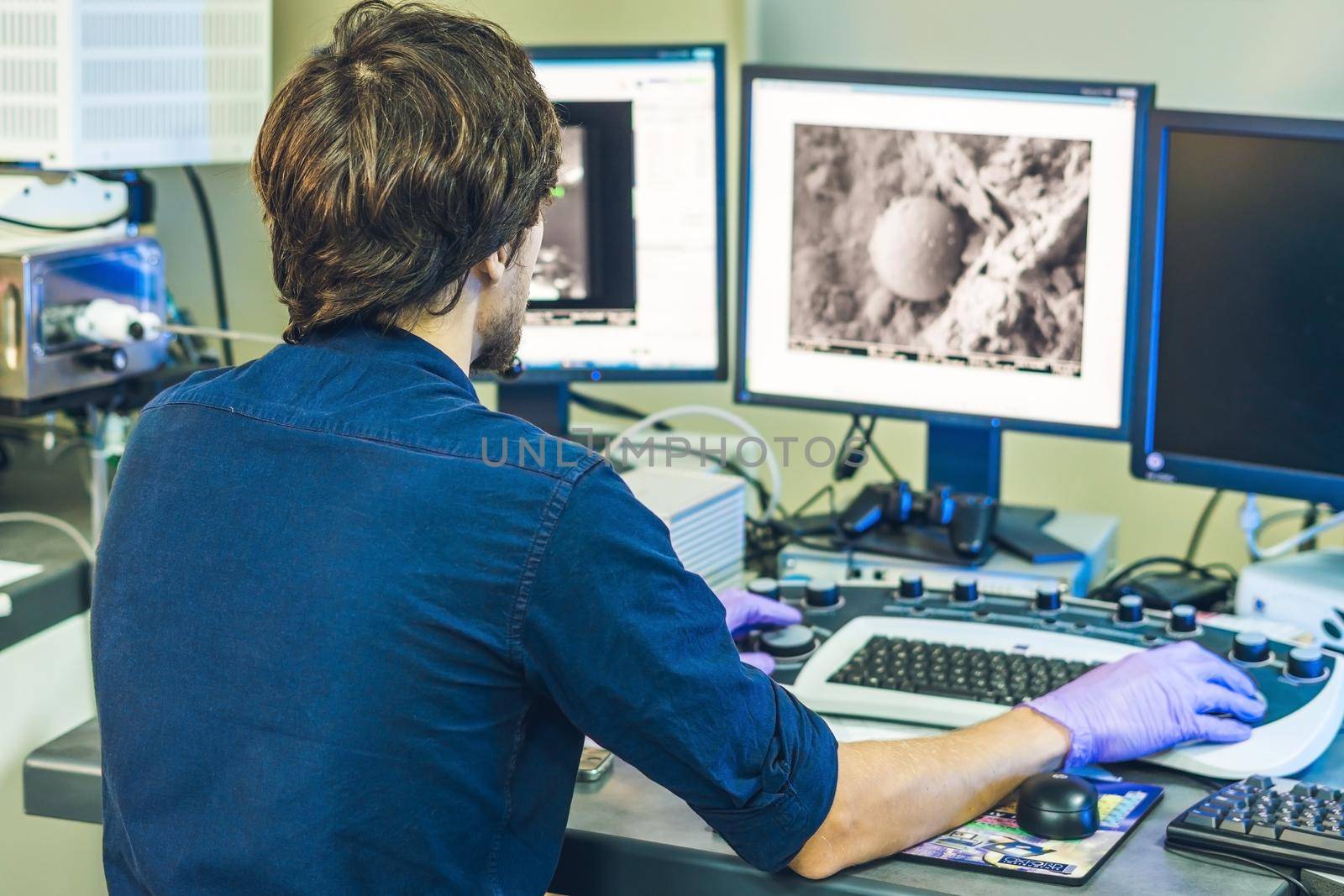 Scientist works at a electron microscope control pannel with two monitors in front of him.