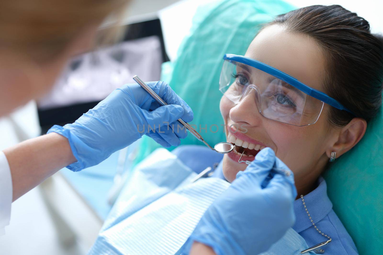 Doctor examining oral cavity of female patient using dental instruments in clinic. Annual preventive dental checkups concept