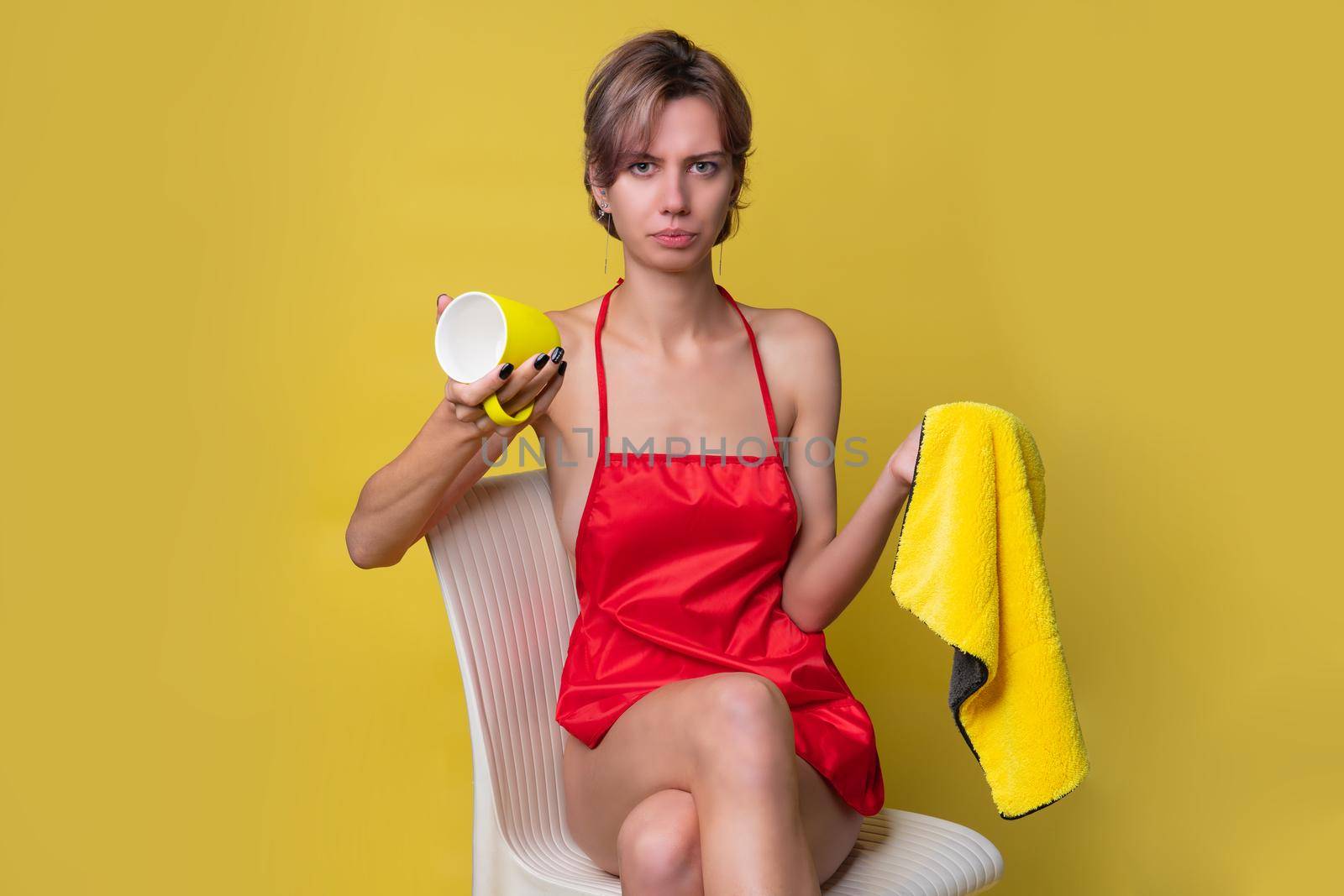 Girl cleans up with a rag and a cup on a yellow background in a red apron housekeeping female hygiene, yellow clean caucasian cleaner, are. tool person, home portrait protective rubber housewife working holding is sitting by 89167702191