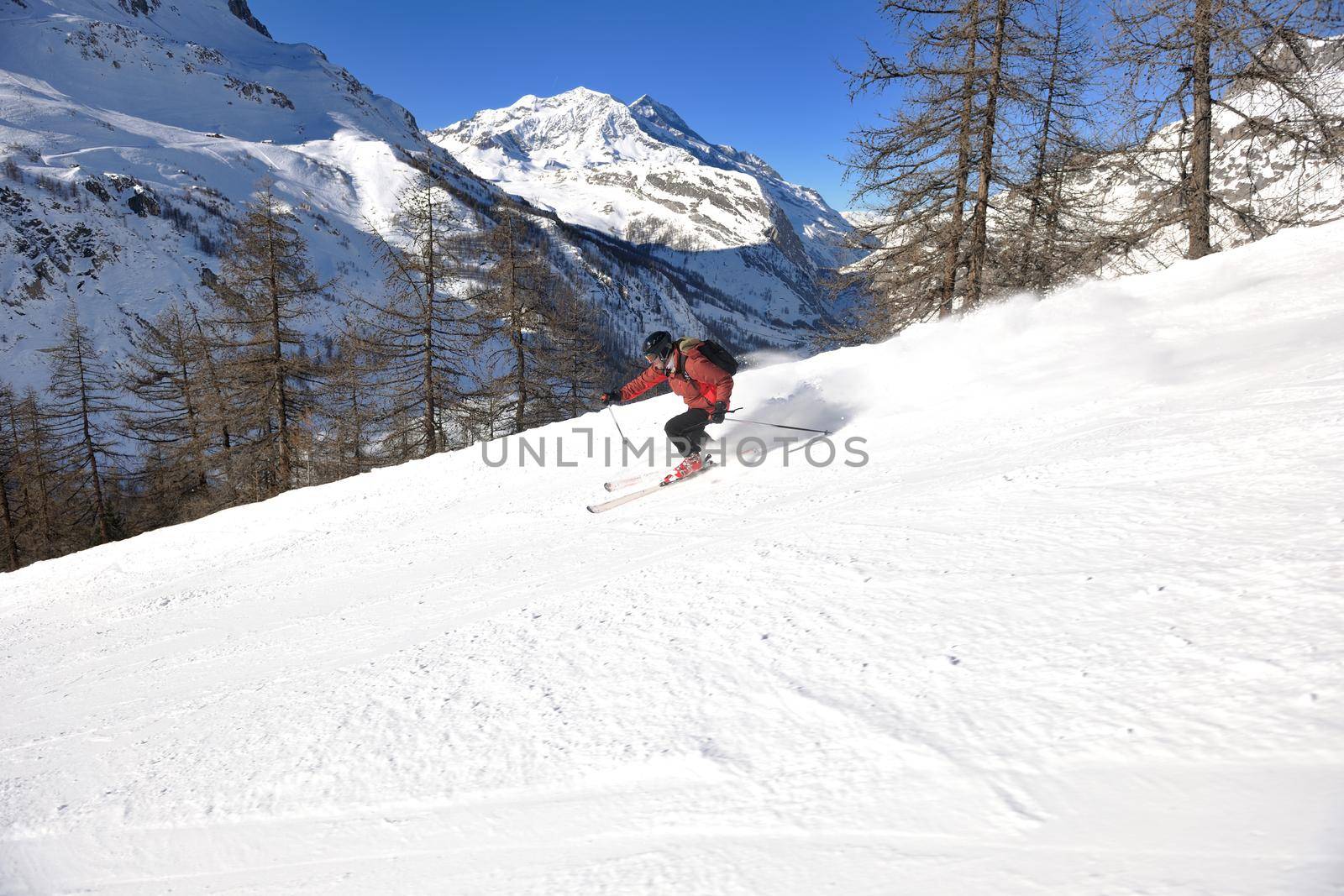 skier skiing downhill on fresh powder snow  with sun and mountains in background