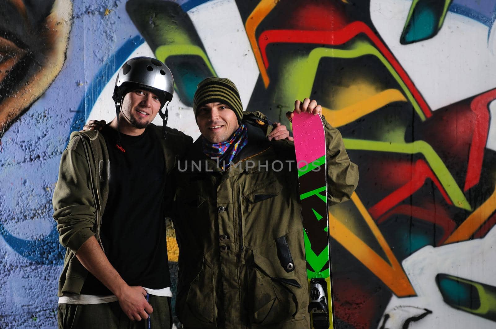 two happy young skiirs standing against colorful background