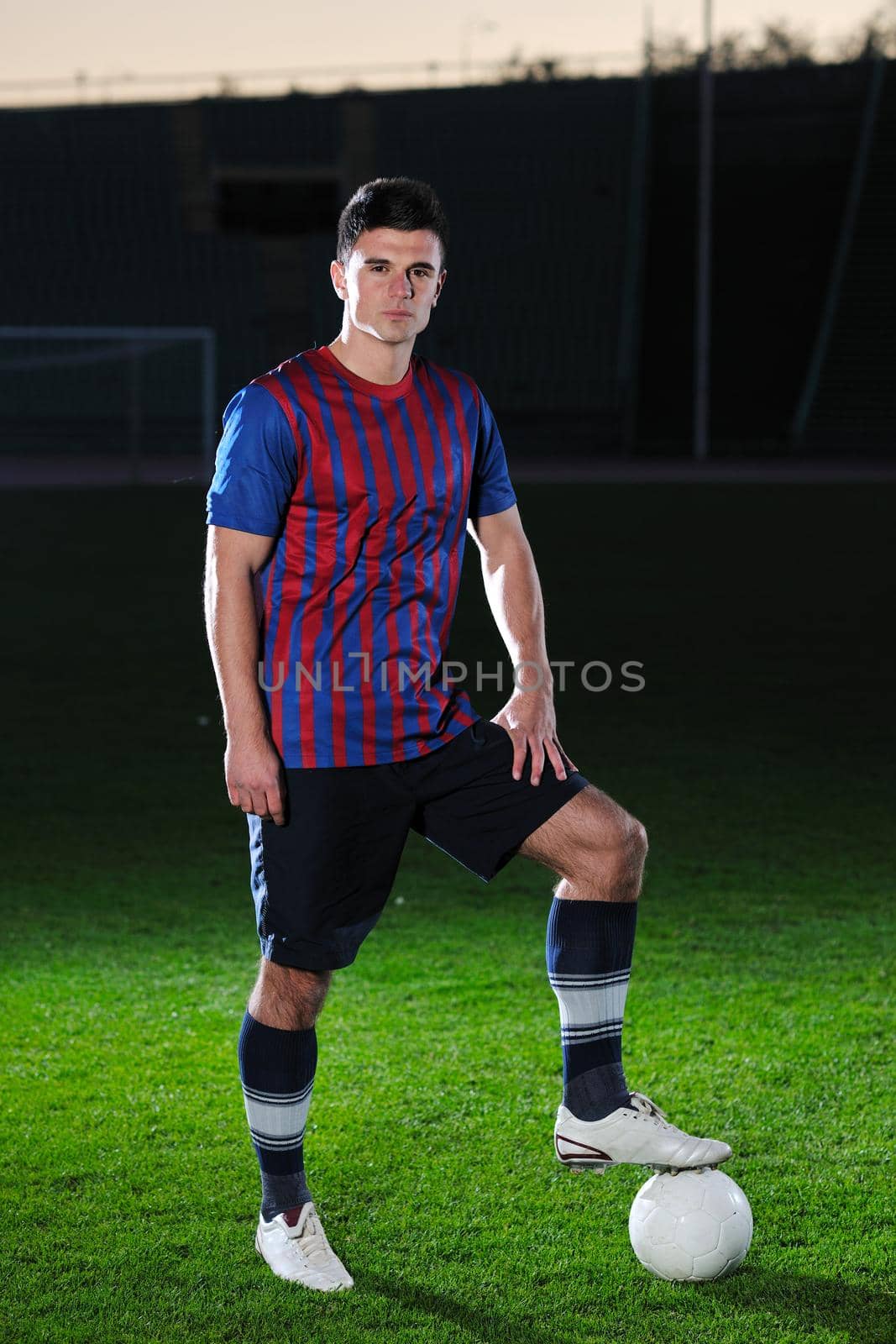 portrait of young handsome soccer player man at football stadium and green grass