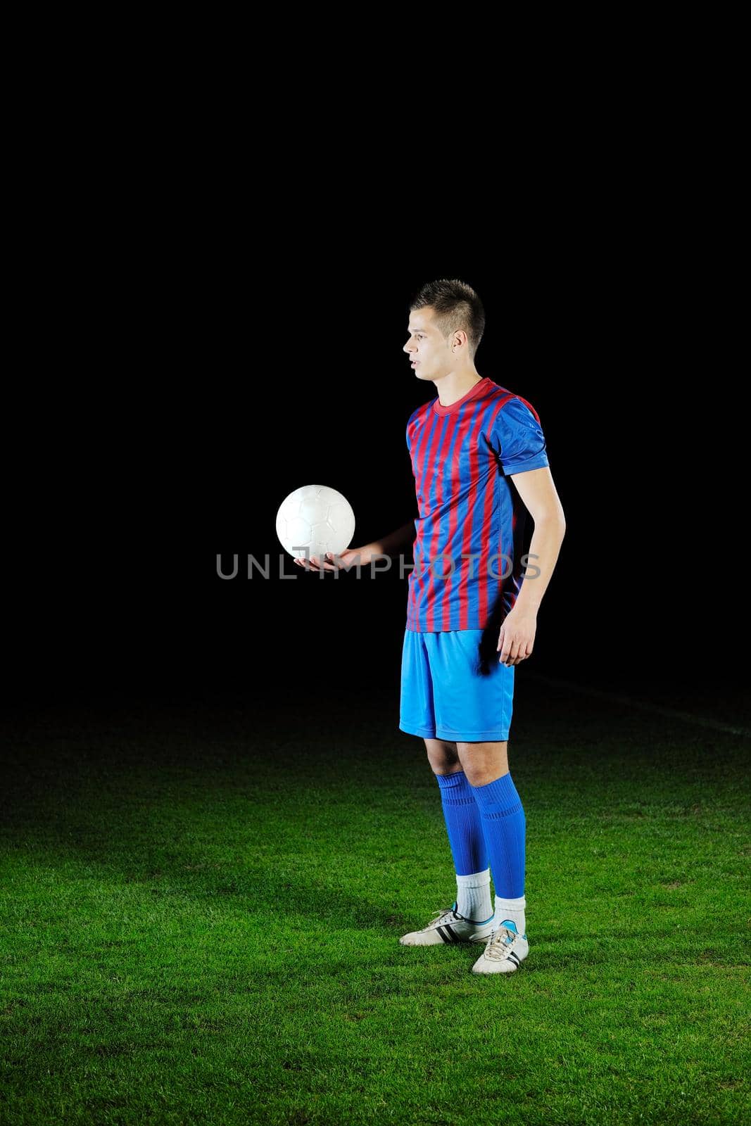 soccer player doing kick with ball on football stadium  field  isolated on black background  in night