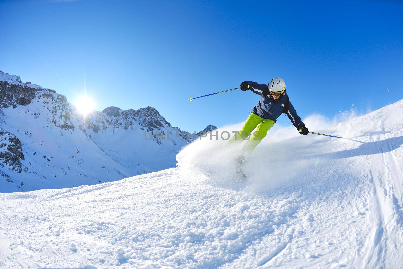 skier skiing downhill on fresh powder snow  with sun and mountains in background