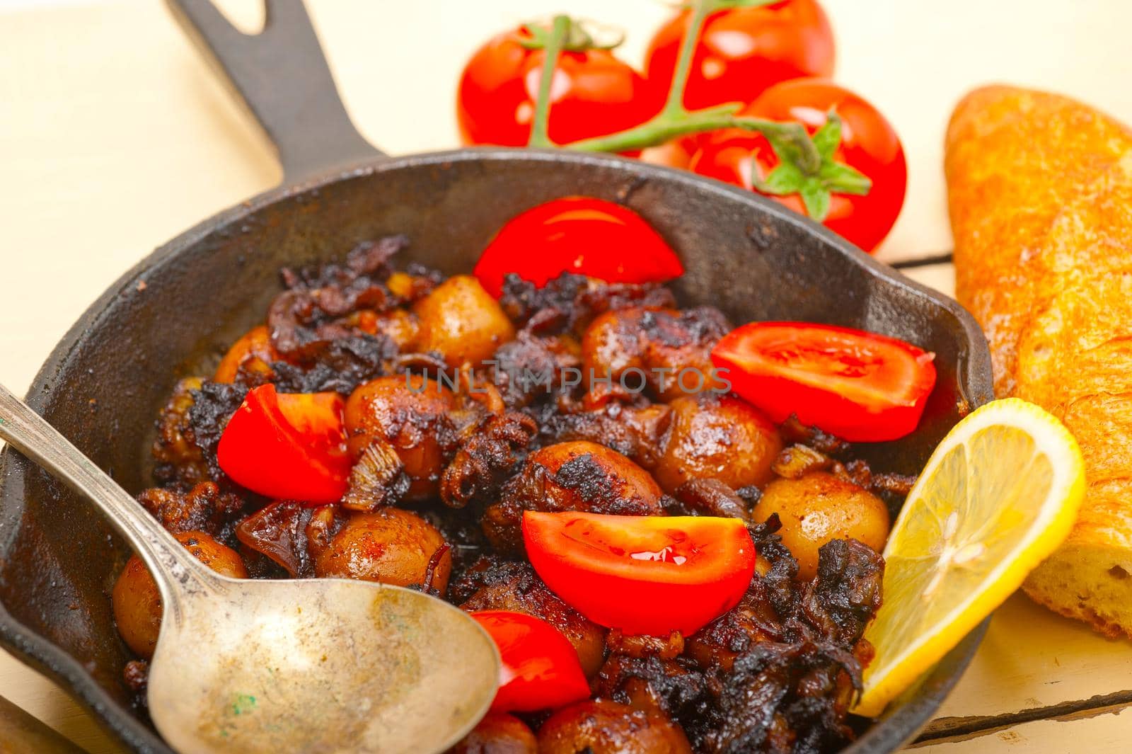 Baby cuttle fish roasted on iron skillet with tomatoes and onions over rustic wood table