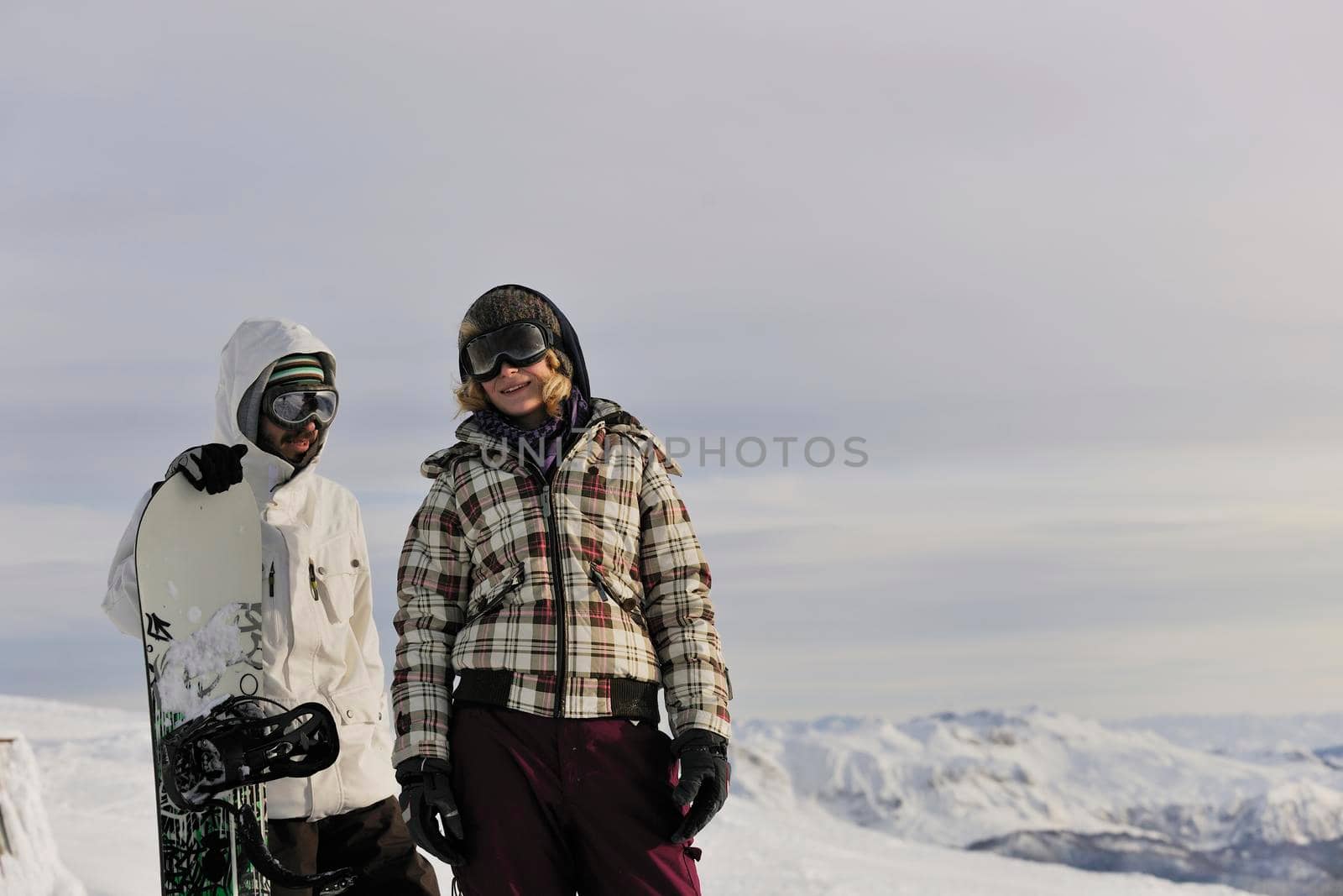 happy young snowboarder couple relax at top of mountain at beautiful sunny winter day