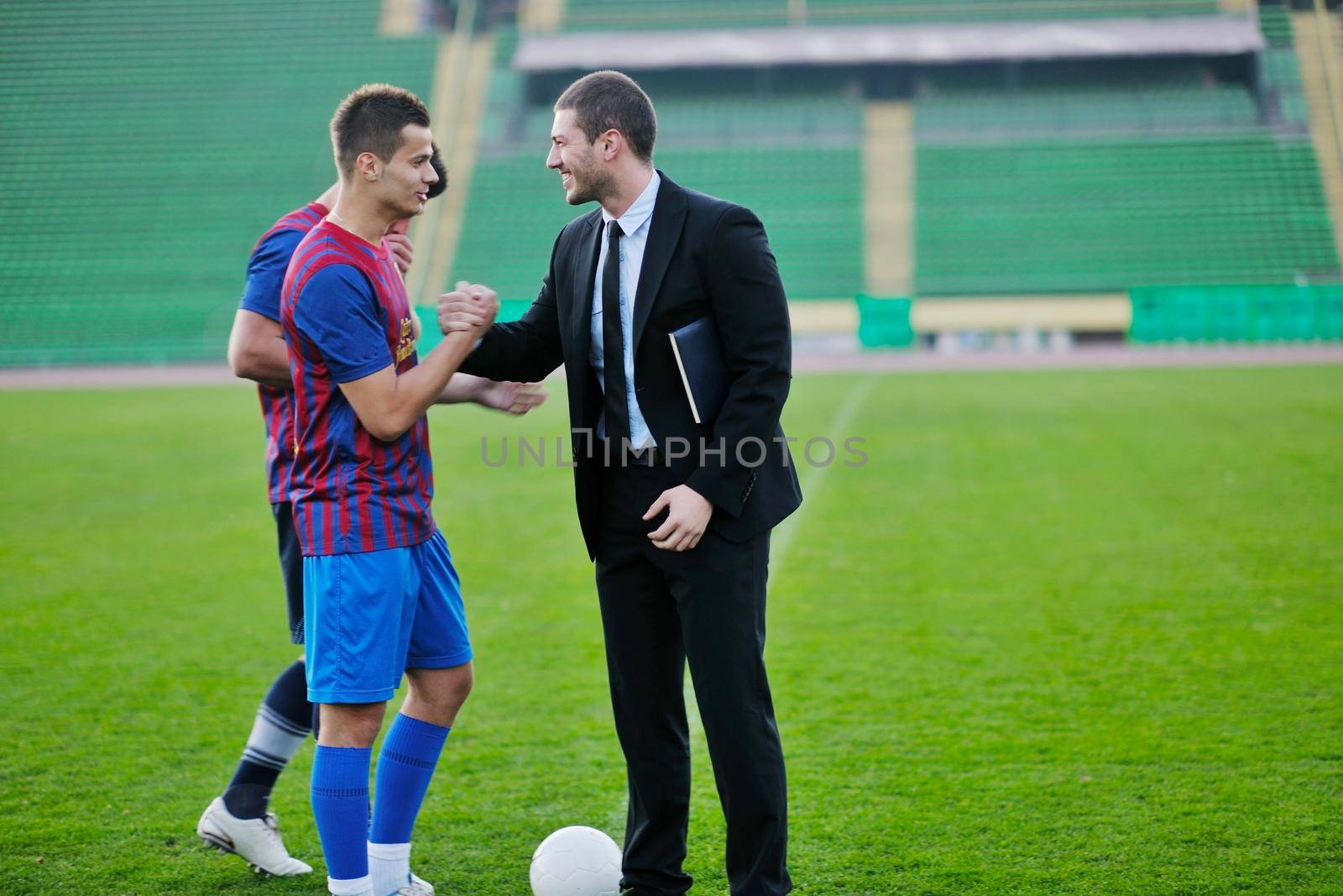 soccer  sport manager in business suit coach and football player on stadium with green grass and white ball