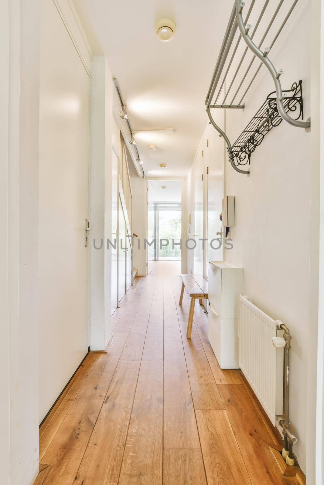A long corridor with in modern apartment with wooden floor and white walls. Interior of contemporary flat in minimal style with spacious hallway with white walls