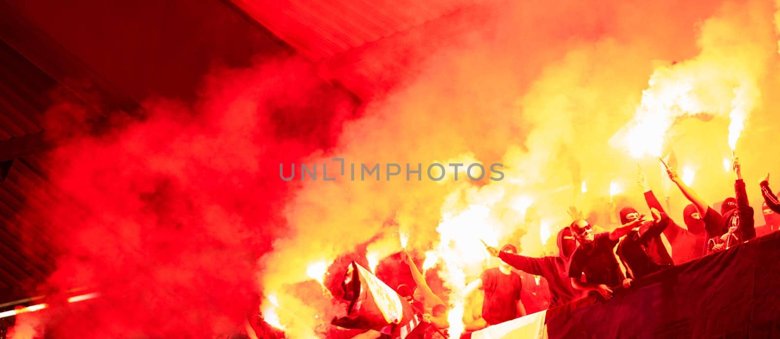 football hooligans with mask holding torches in fire while supporting their favorite team during a match at stadium