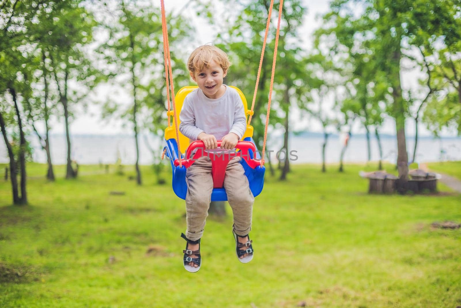 happy little boy riding on a swing in a park by galitskaya