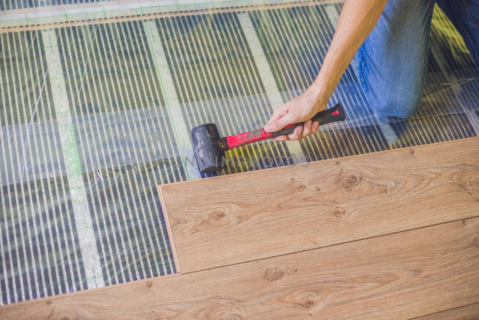 Man installing new wooden laminate flooring. infrared floor heating system under laminate floor by galitskaya