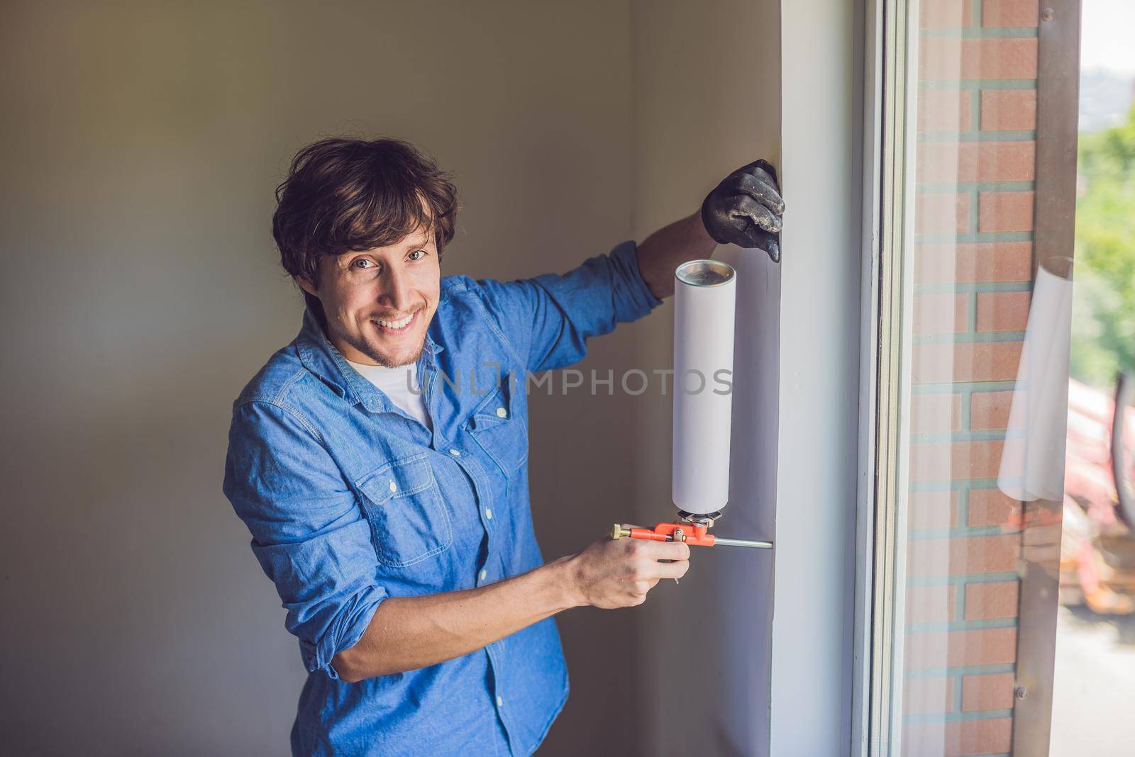 Man in a blue shirt does window installation. Using a mounting foam.