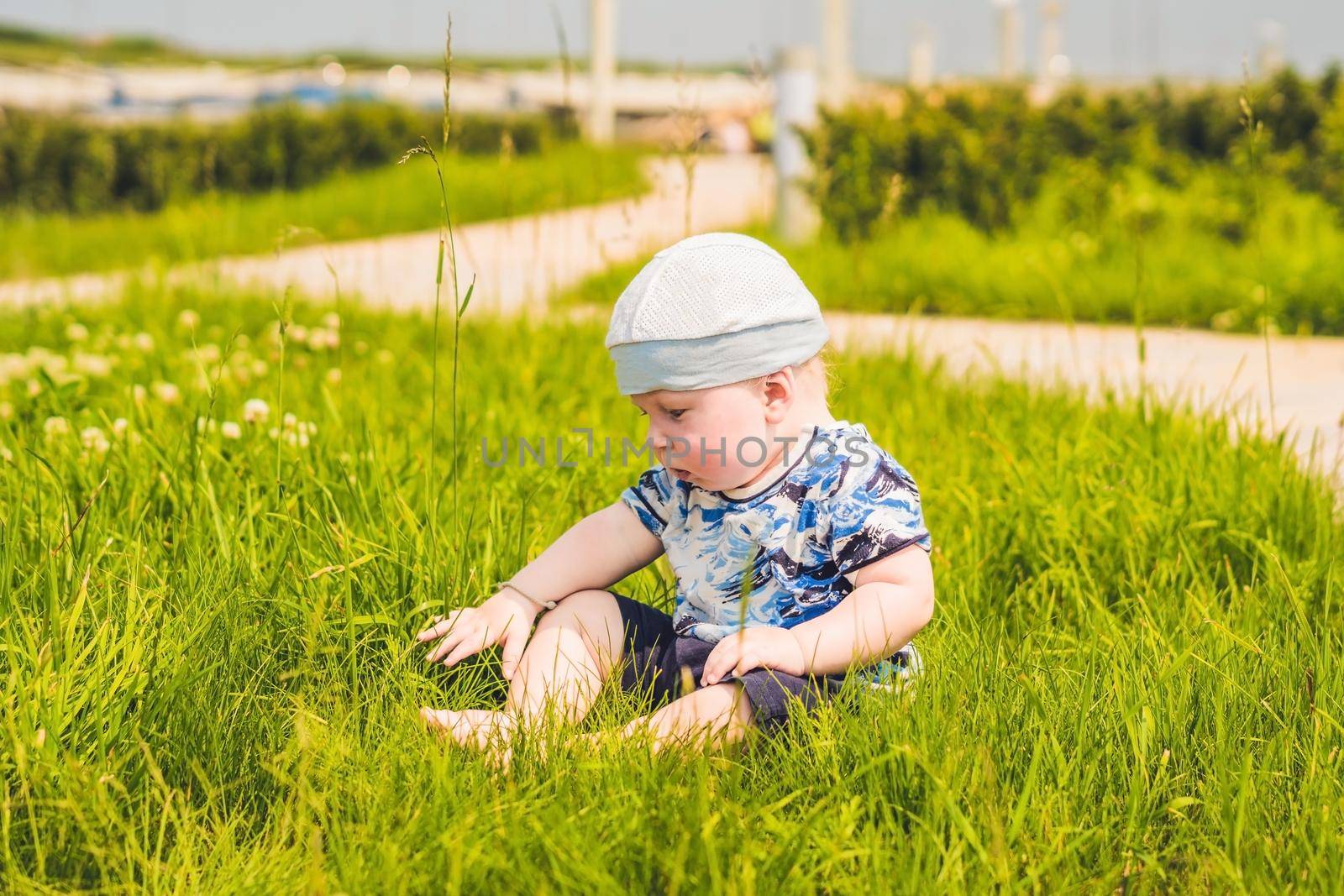 Cute little toddler baby boy child playing in the park on grass at day time. He having fun on the garden.