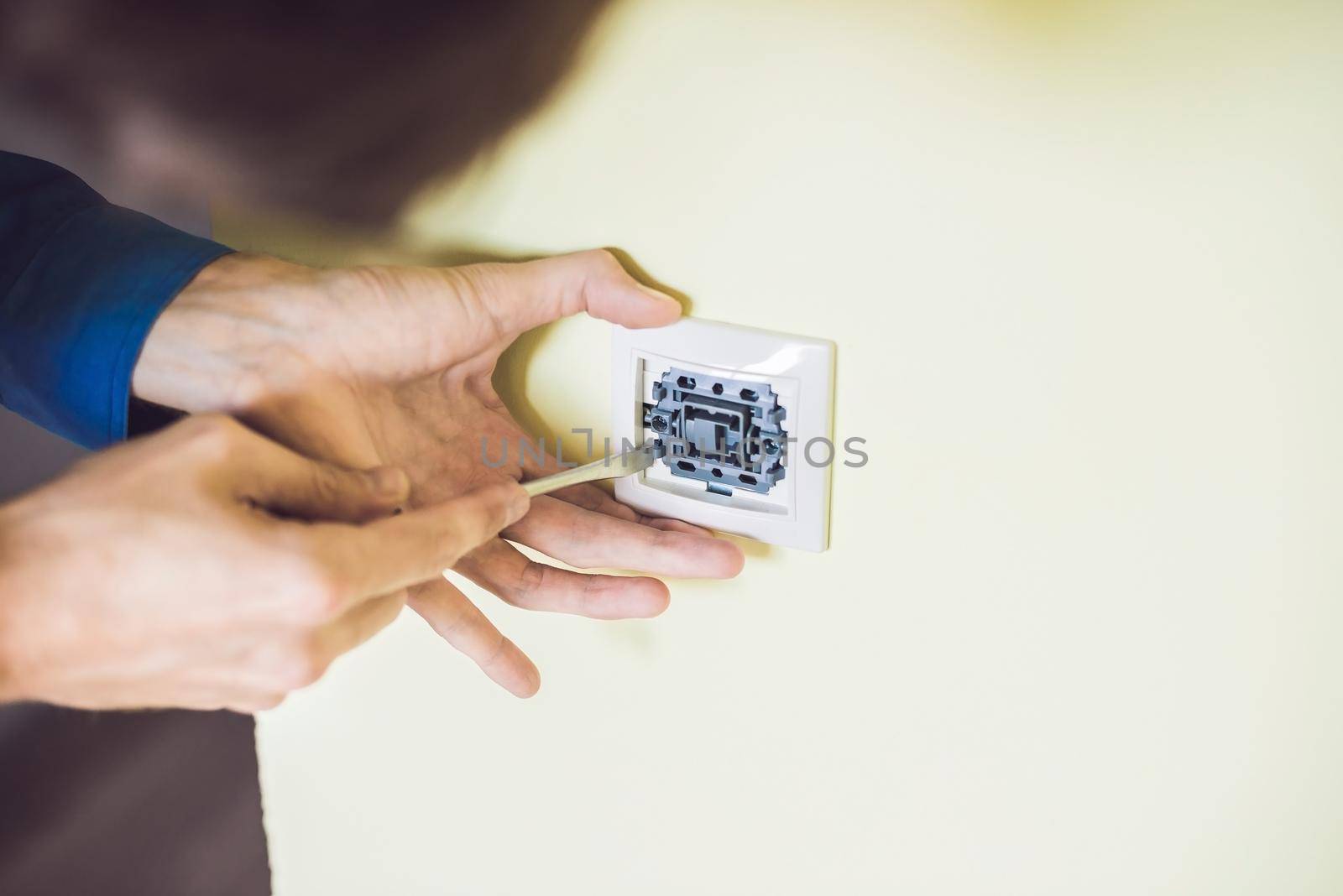 A young electrician installing an electrical switch in a new house by galitskaya