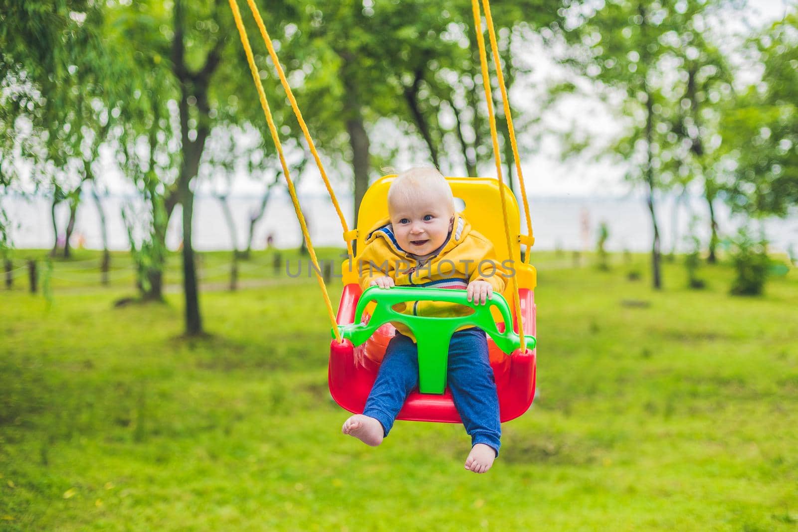 happy little boy riding on a swing in a park by galitskaya