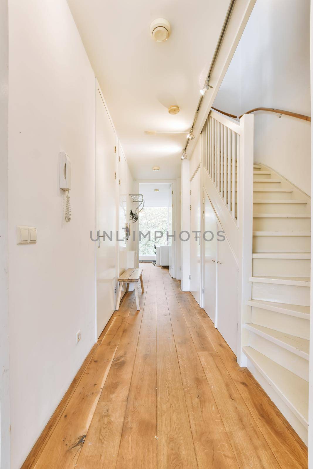 Interior of the narrow corridor with telephone hanging on the wall against stairway in daylight