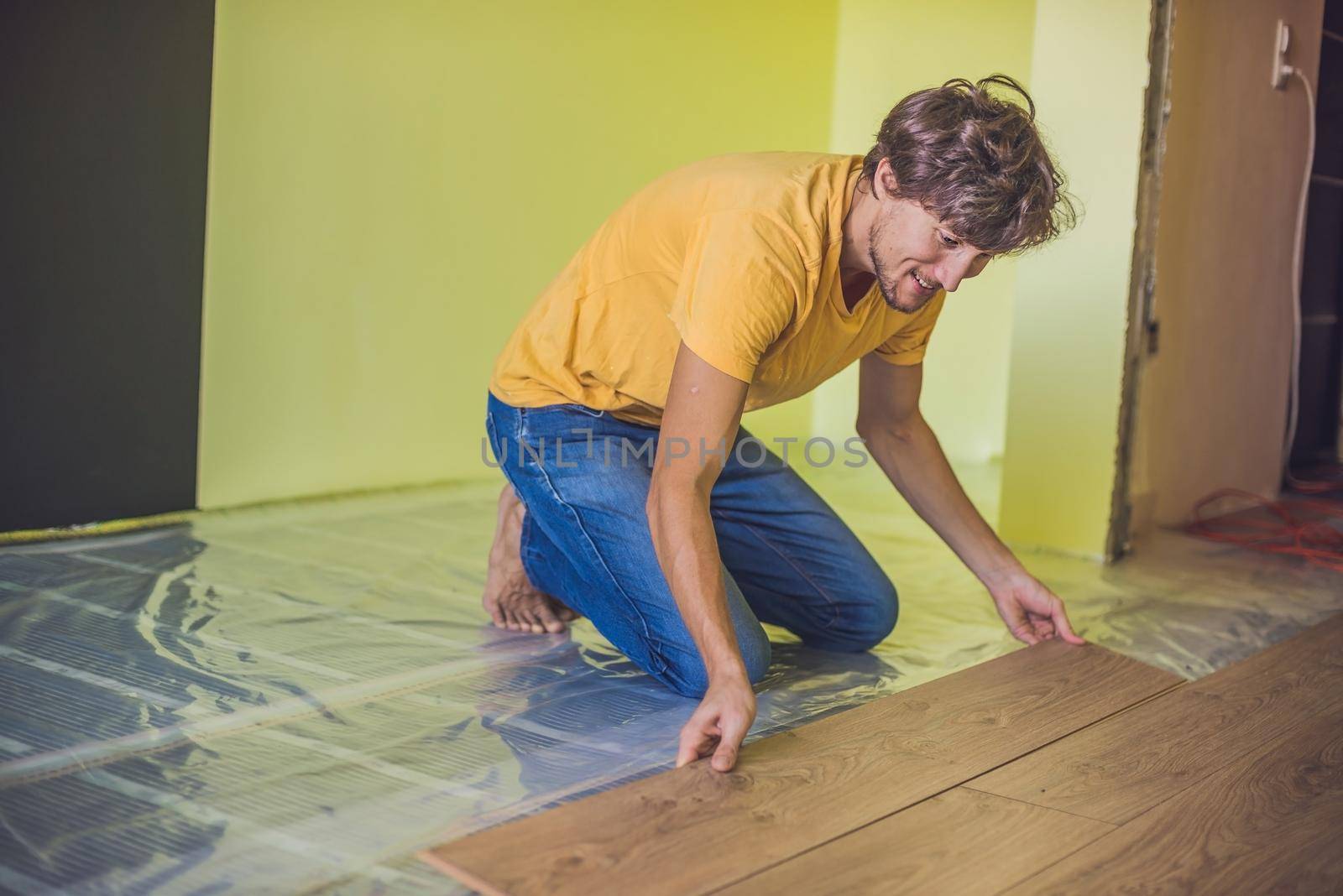 Man installing new wooden laminate flooring. infrared floor heating system under laminate floor by galitskaya