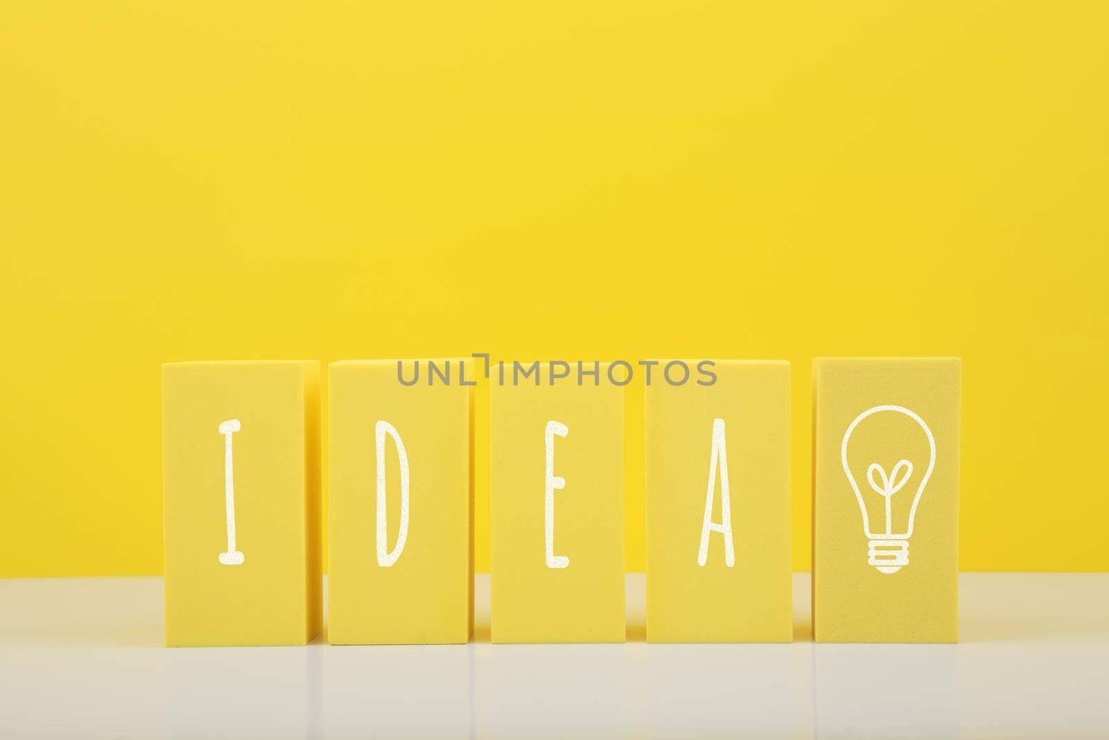 Concept of idea, creativity, start up or brainstorming. The word idea and bulb drawn on yellow toy blocks against bright yellow background with copy space.