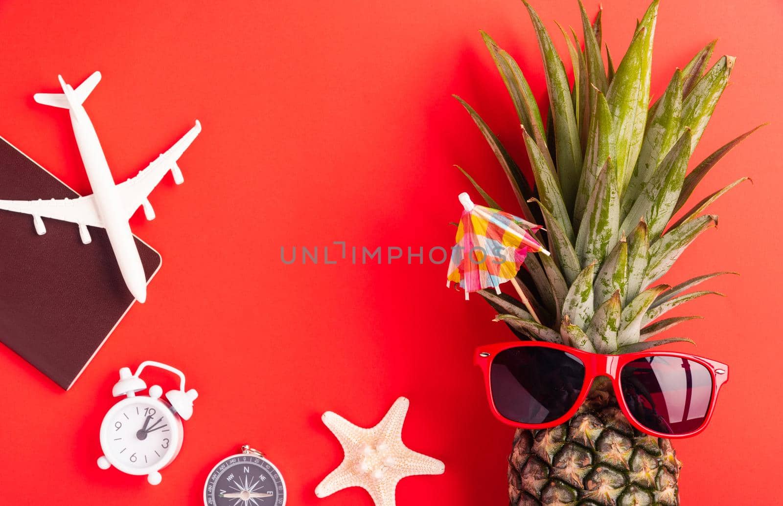 Summer Pineapple Day Concept, Top view flat lay of funny pineapple wear red sunglasses, model plane, starfish, passport and clock alarm isolated on red background, Holiday summertime in tropical