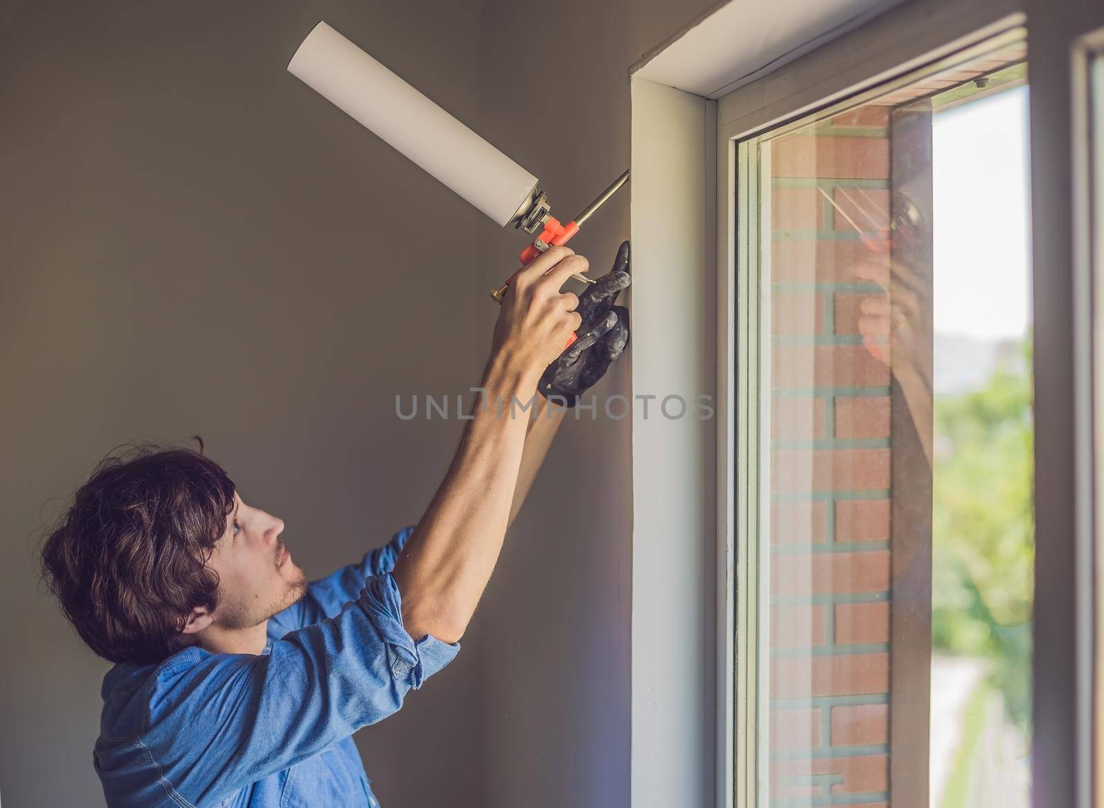 Man in a blue shirt does window installation. Using a mounting foam.