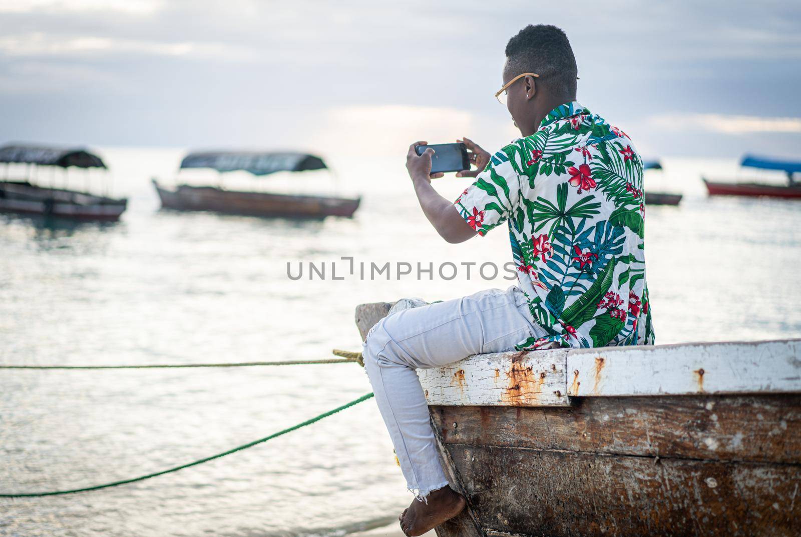 Young black man sitting on boat taking selfie by Zurijeta