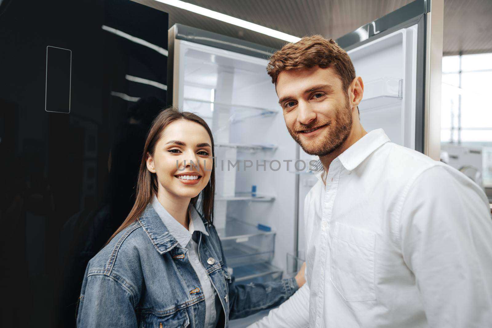 Young couple selecting new refrigerator in household appliance store, close up