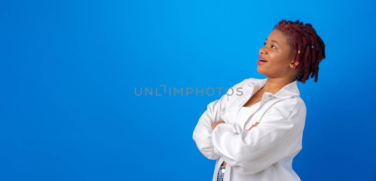 Young afro woman in white shirt looking up at copy space for advertising on blue studio background