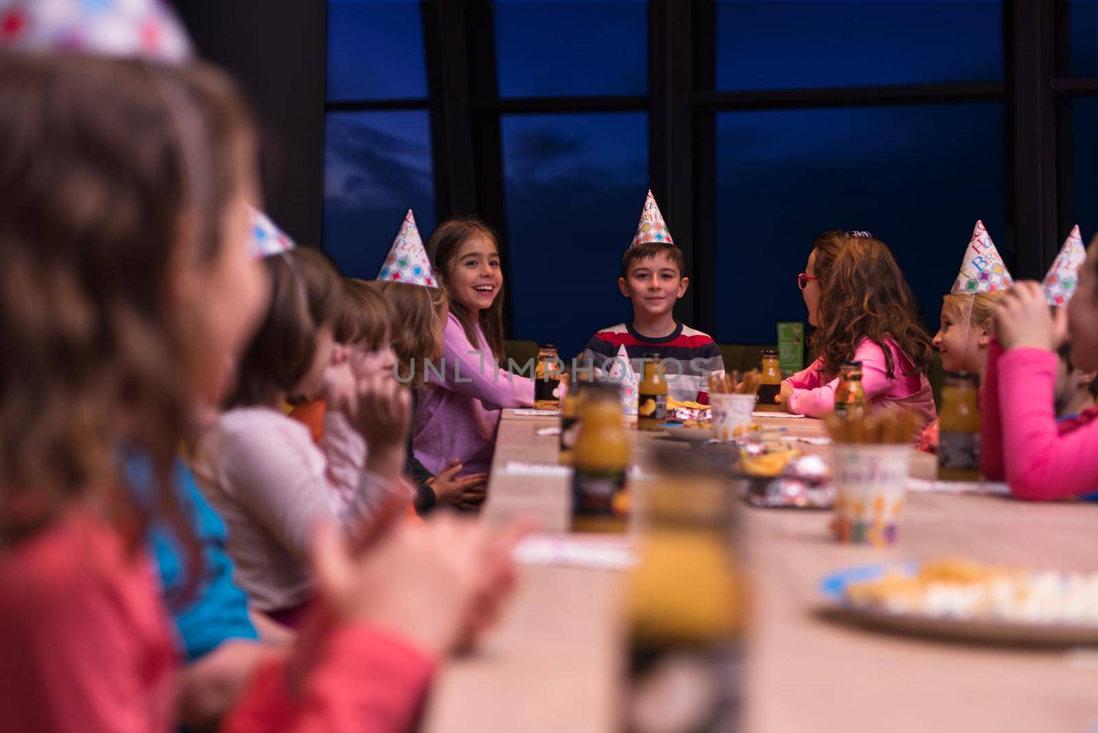 young happy boy and group of his friends having birthday party with a night sky through the windows in the background