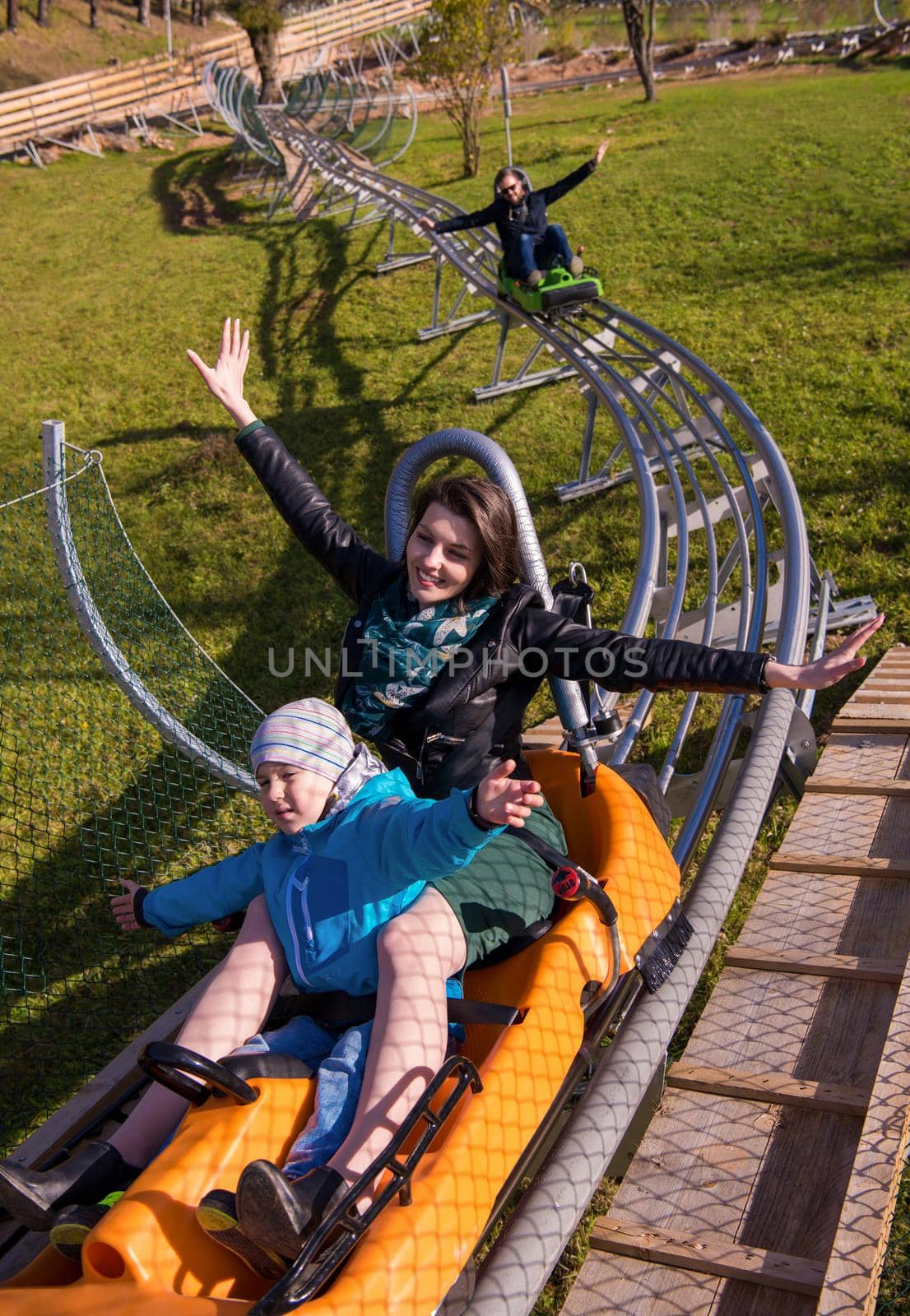 Excited young mother and son driving on alpine coaster while enjoying beautiful sunny day in the nature