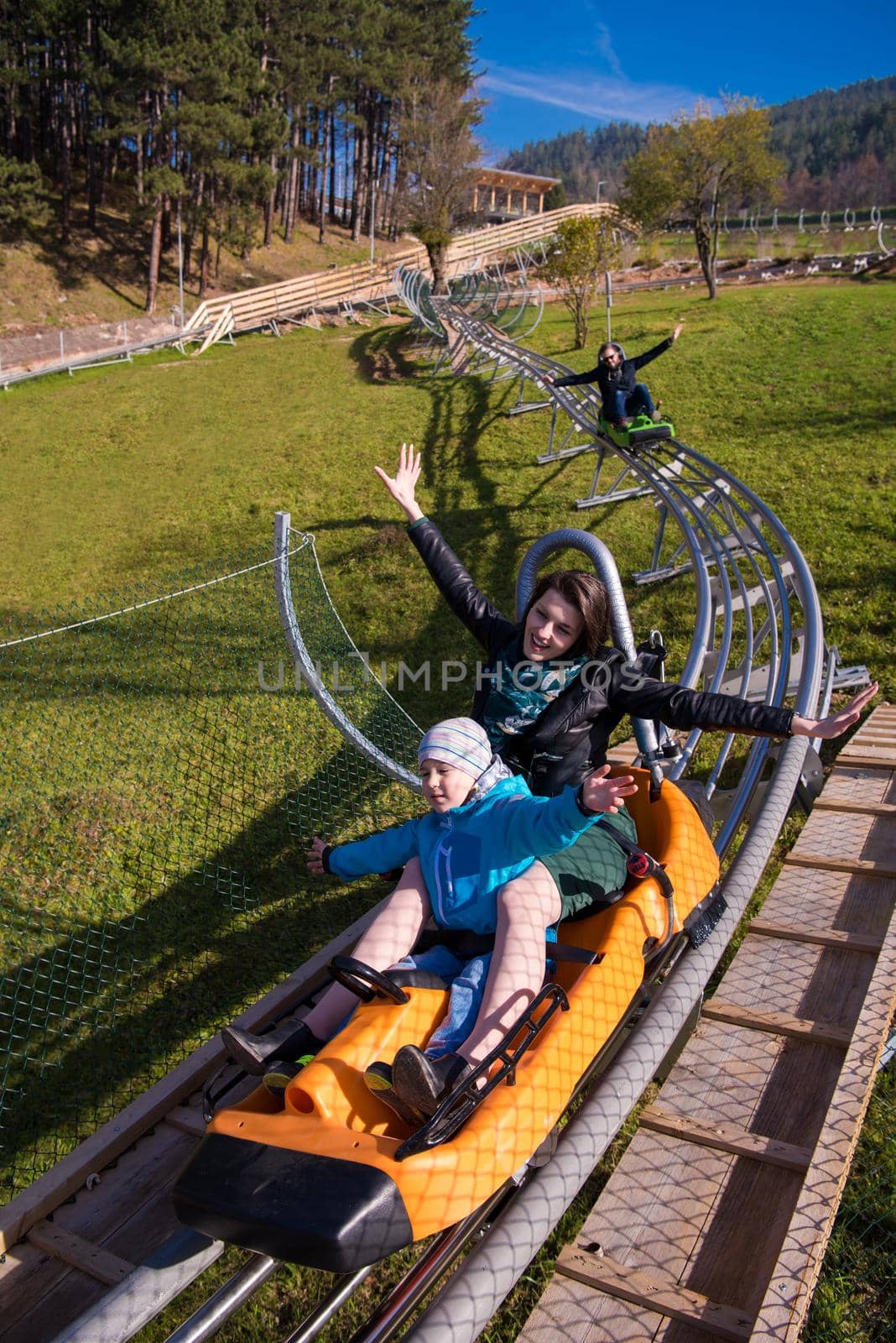 Excited young mother and son driving on alpine coaster while enjoying beautiful sunny day in the nature