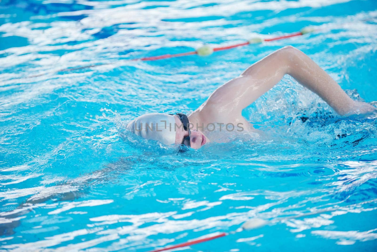 Happy muscular swimmer wearing glasses and cap at swimming pool and represent health and fit concept